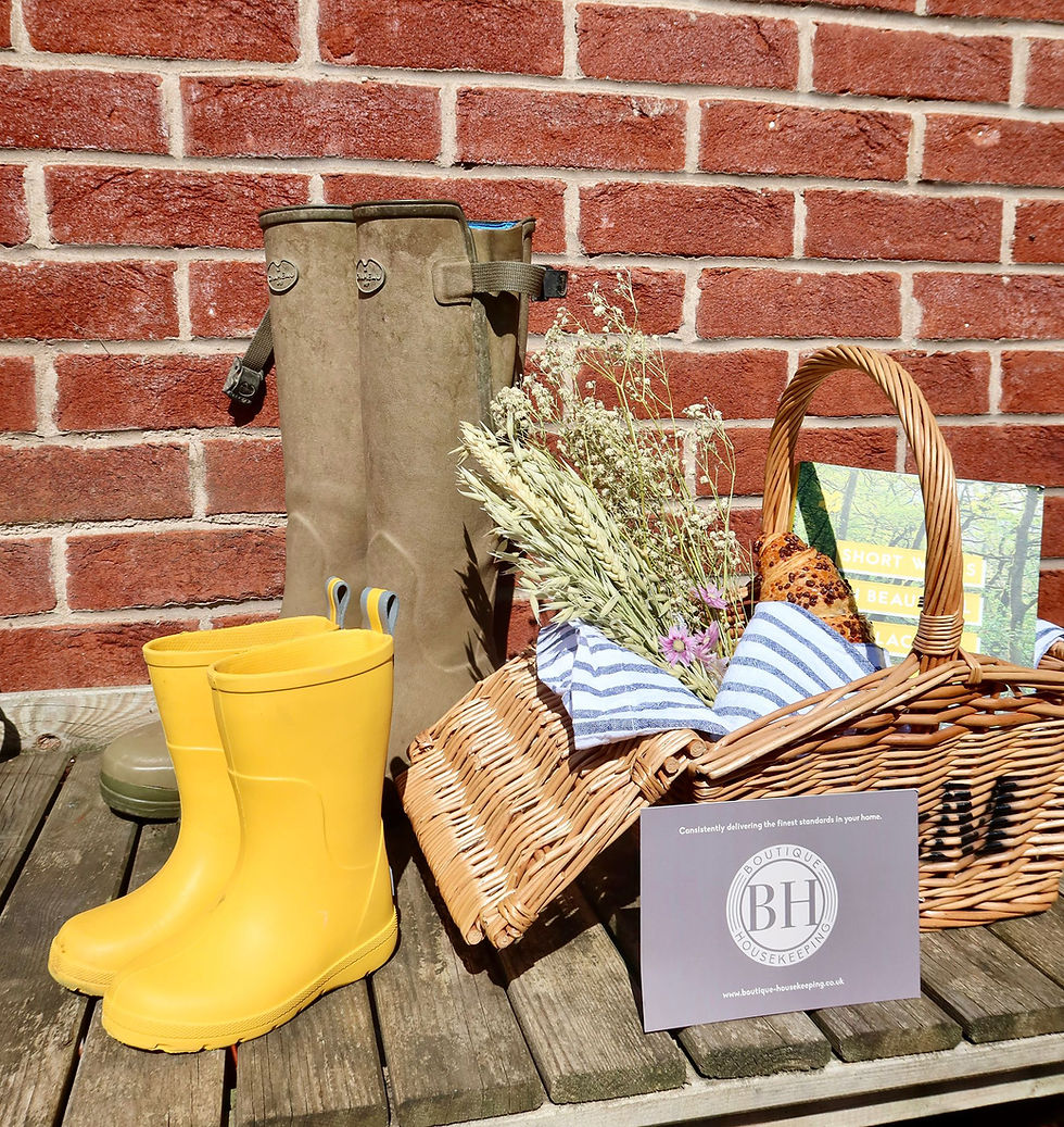 Yellow rain boots, wicker basket with bread and dried flowers, and olive utility boots beside a BH Boutique Housekeeping card.