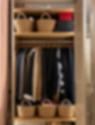 Neatly hung coats, woven baskets on shelves, and stacked boxes in a warm-toned, organised wardrobe