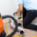 A Longman's Cleaning Services technician is using tools to clean out a dryer vent at the wall. On the floor is dryer hosing and a vacuum tube is showing.