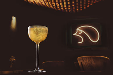 Professionelle Cocktail- und Getränkefotografie: Ein eleganter Gold-Cocktail im stilvollen Bar-Ambiente, atmosphärisch inszeniert mit warmem Licht und modernem Neon-Design. Hochwertige Food Fotografie für Bars, Restaurants, Marken und Social Media – perfekt für Branding, Werbung und starke visuelle Präsenz.