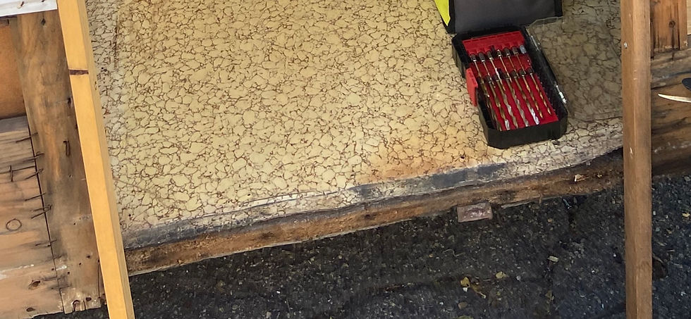 Toolbox with red and black drill bits on a cracked beige linoleum trailer floor. No visible text, outdoor setting.