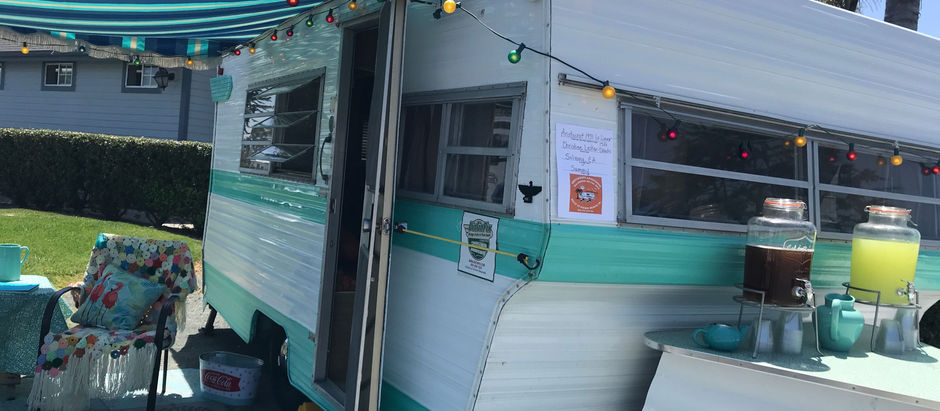 Eye-level view of a shiny restored mint green and white vintage trailer parked in a sunny campground