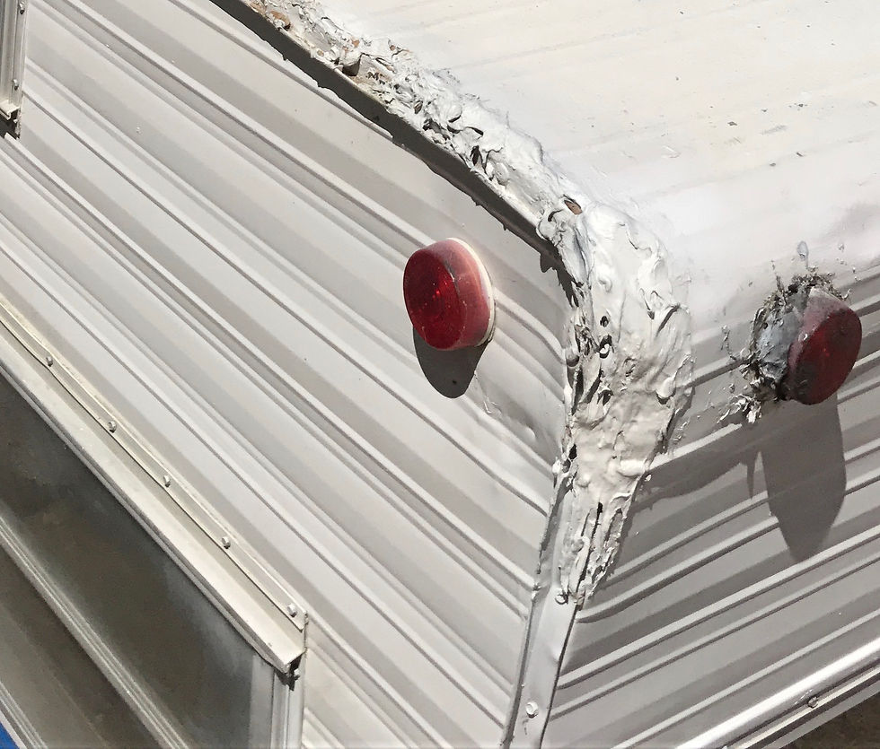 Close-up of a trailer corner showing red lights and patched white sealant. The surface is ribbed metal with signs of aging and wear.