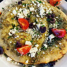 Toasted flat bread topped with tomatoes, olives, white cheese, and green herbs