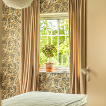 Sovrum med stort fönster och blommig tapet.