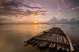 Bamboo raft on calm water at sunset, with vibrant orange and purple sky. Reflective mood with clouds and distant horizon. No visible text.