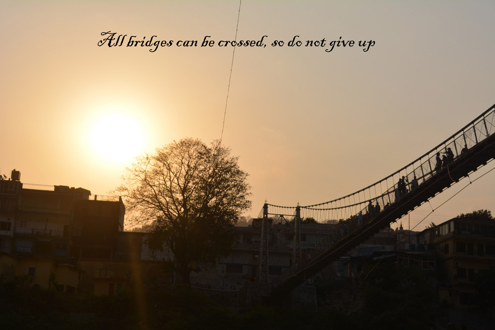 Sunset over a suspension bridge with silhouetted people crossing. Text reads "All bridges can be crossed, so do not give up."