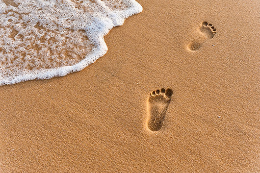 Footprints in sand near ocean wave