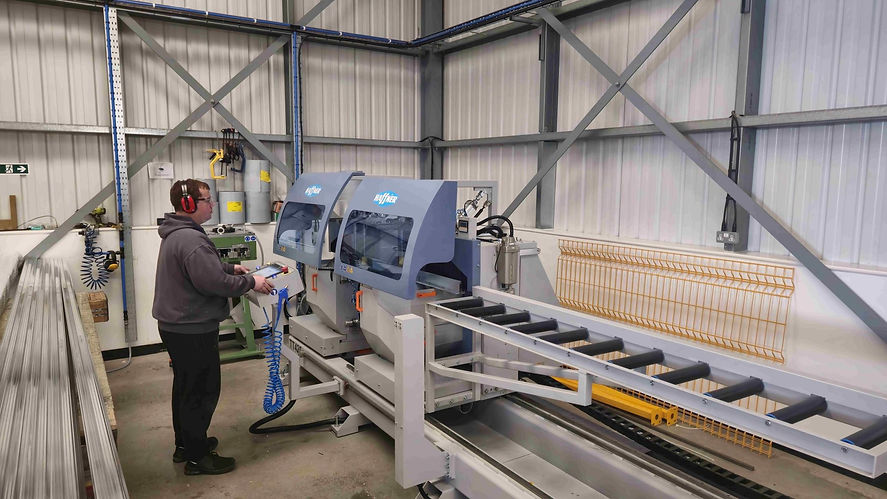 Staff member using a saw in the Contech Conservatories factory to cut an aluminium roof profile with precision.
