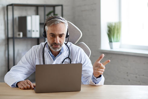 portrait-senior-grey-haired-male-doctor-his-office-using-laptop-video-chat-with-patient-on