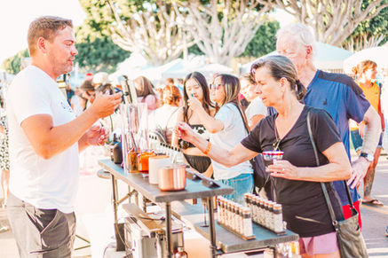 Vendor assisting customer at Dreamers Markets, selling products under sunny skies.