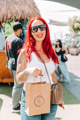 Woman with red hair and sunglasses holding a shopping bag at Dreamers Markets.