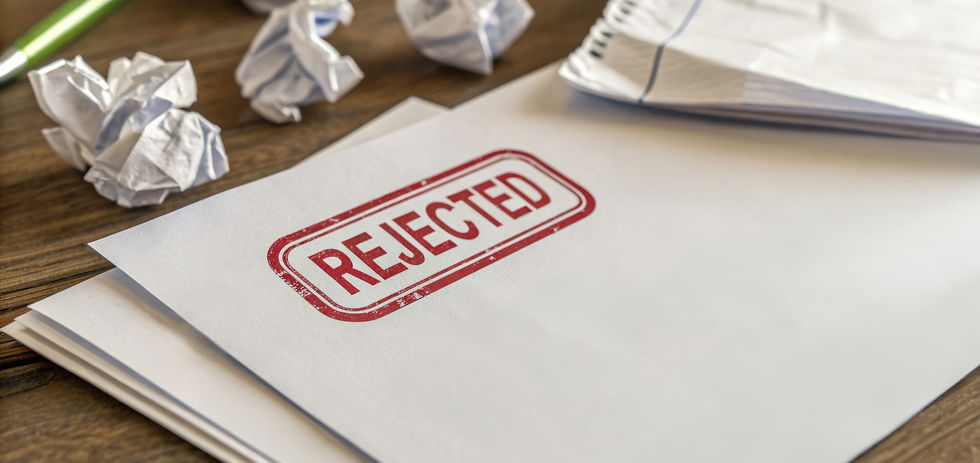 Stack of papers stamped "REJECTED" in red on a wooden desk with crumpled balls of paper and a pen, conveying a mood of disappointment.