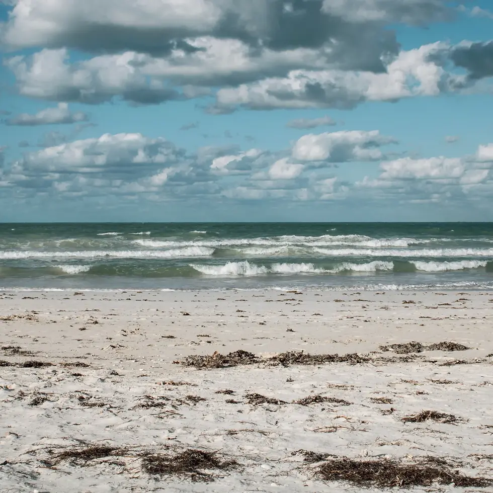 A sunny beach with white clouds and waves rolling in