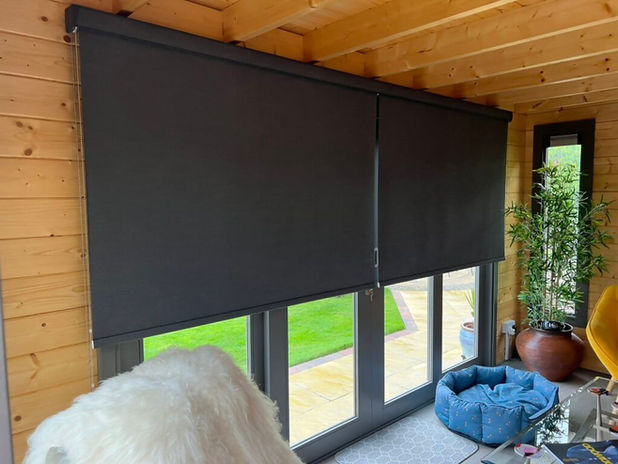 Dark grey roller blinds covering a large window in a garden room