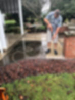 Employee of Sanders Cleaning Service operates a hand-held professional pressue washer cleaning a patio area of a residential home.