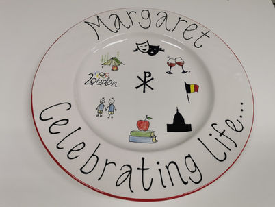 A personalised hand painted plate with Margaret, Celebrating life and lot of little paintings of activities including theature, camping, reading, a flag etc.