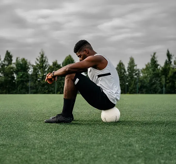 Kofi Schulz sitting on a football with his head down during a training session, reflecting on the habits and mindset that influence performance on the pitch.