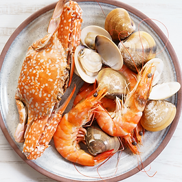 Prato de frutos do mar contendo um caranguejo cozido, camarões rosados inteiros e várias conchas de mariscos abertas e fechadas, servido sobre um prato rústico em fundo branco.