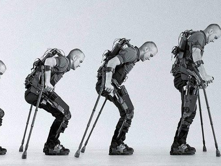 Sequência em preto e branco mostrando um homem usando um exoesqueleto. Ele aparece passando da posição sentada em uma cadeira de rodas para ficar em pé e caminhar com o auxílio de muletas, demonstrando o funcionamento do equipamento.