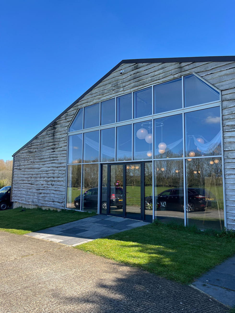 Modern barn-like building with a large glass facade reflecting parked cars and hanging lights under a clear blue sky