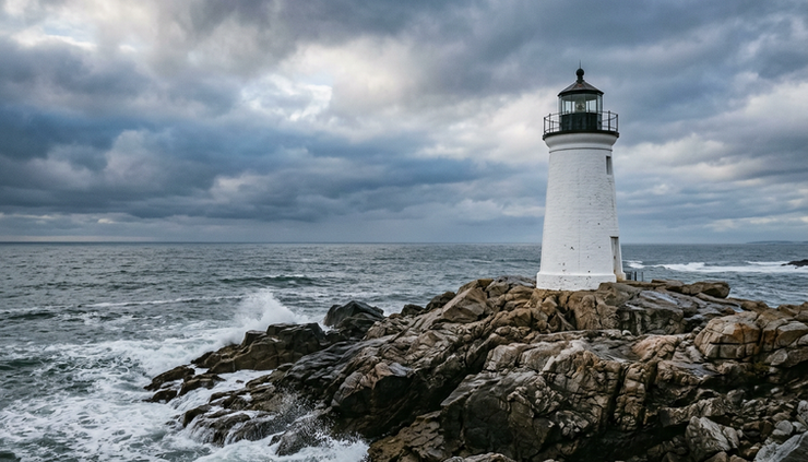 Eye-level view of a lighthouse standing on a rocky coast under a cloudy sky.