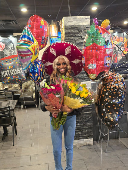 Natalie Black celebrating in a sombrero, holding flowers and balloons.