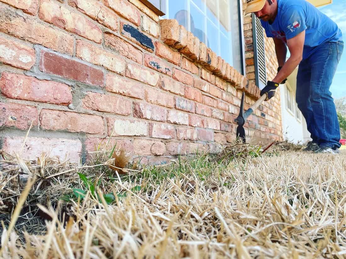 Digging at a brick foundation for termite treatment — Tejas Pest and Weed Control Andrews