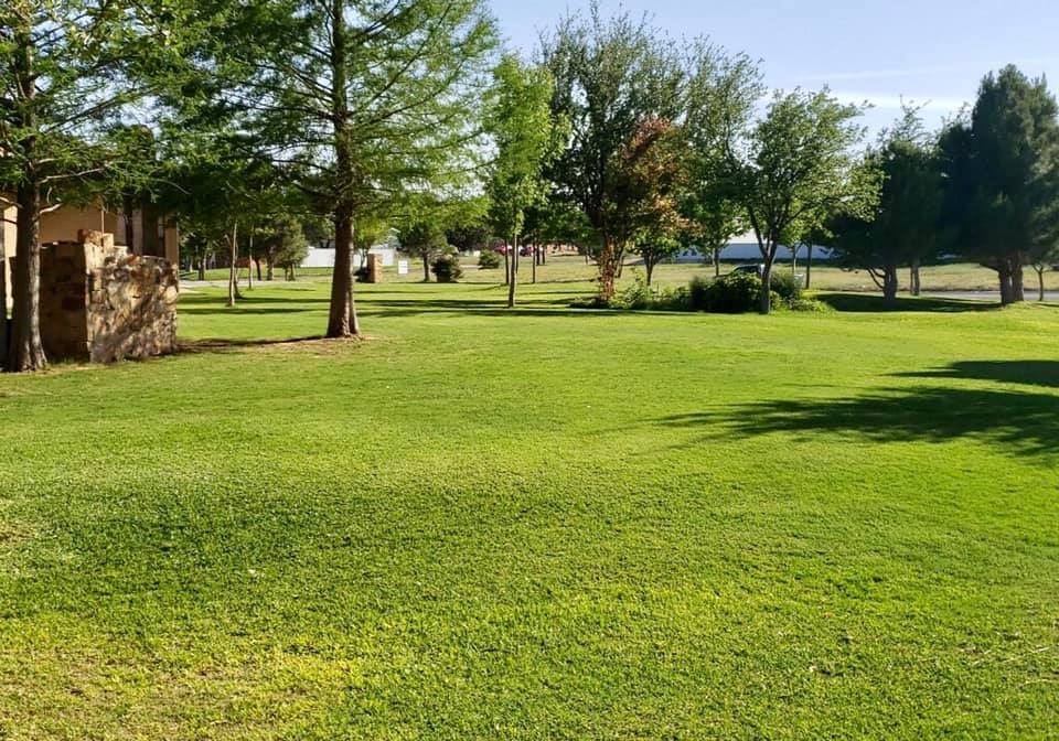 Manicured green lawn with mature trees and stone entry pillar under West Texas sky — Tejas Pest and Weed Control commercial curb appeal