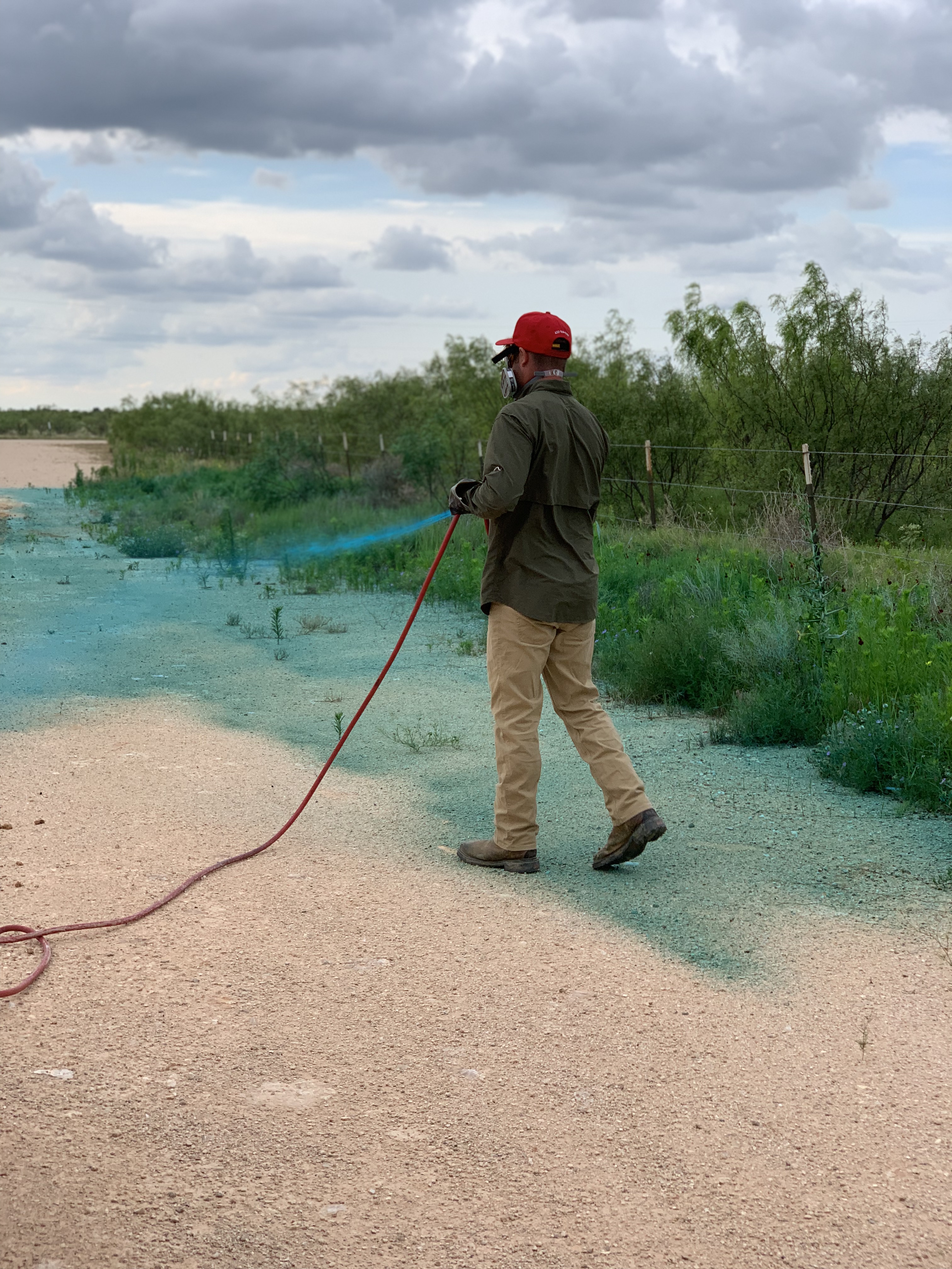 Tejas Pest and Weed Control technician treating ground near West Texas shrubs and trees for Big Spring TX tree care