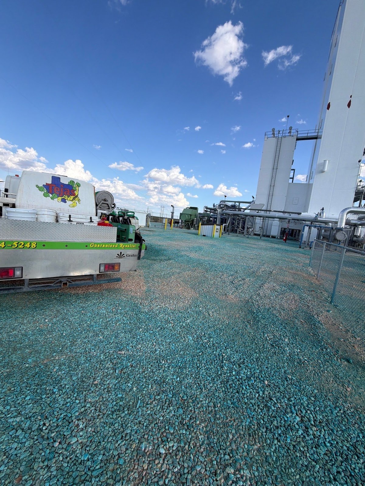 Tejas Pest and Weed Control branded truck at Andrews industrial plant with white silos; gravel lot with turquoise herbicide coverage — Permian Basin brush and yard cleanup