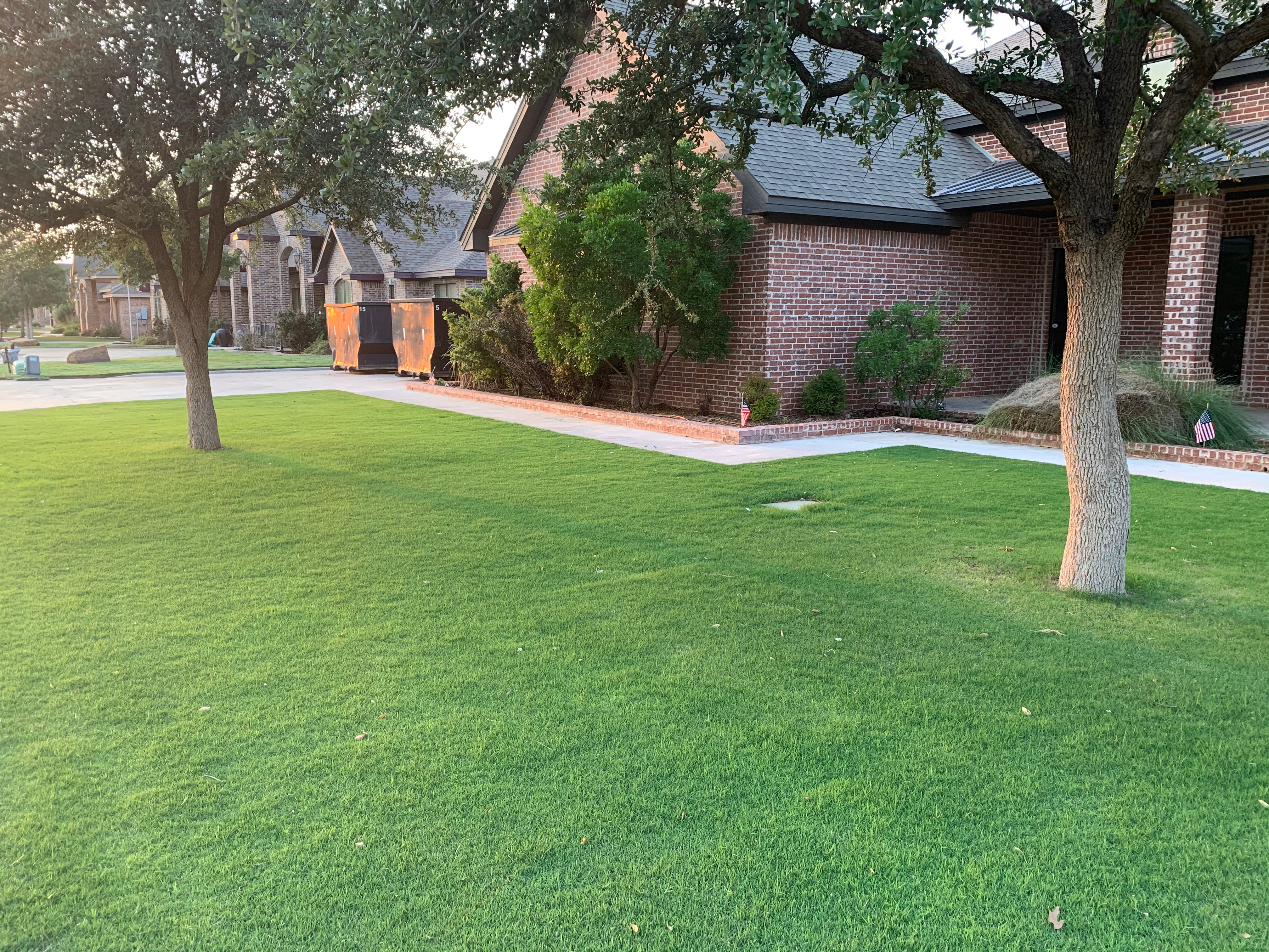 Green residential Bermuda lawn with shade trees in front of a brick home — Tejas Pest and Weed Control lawn aeration and fertilizer
