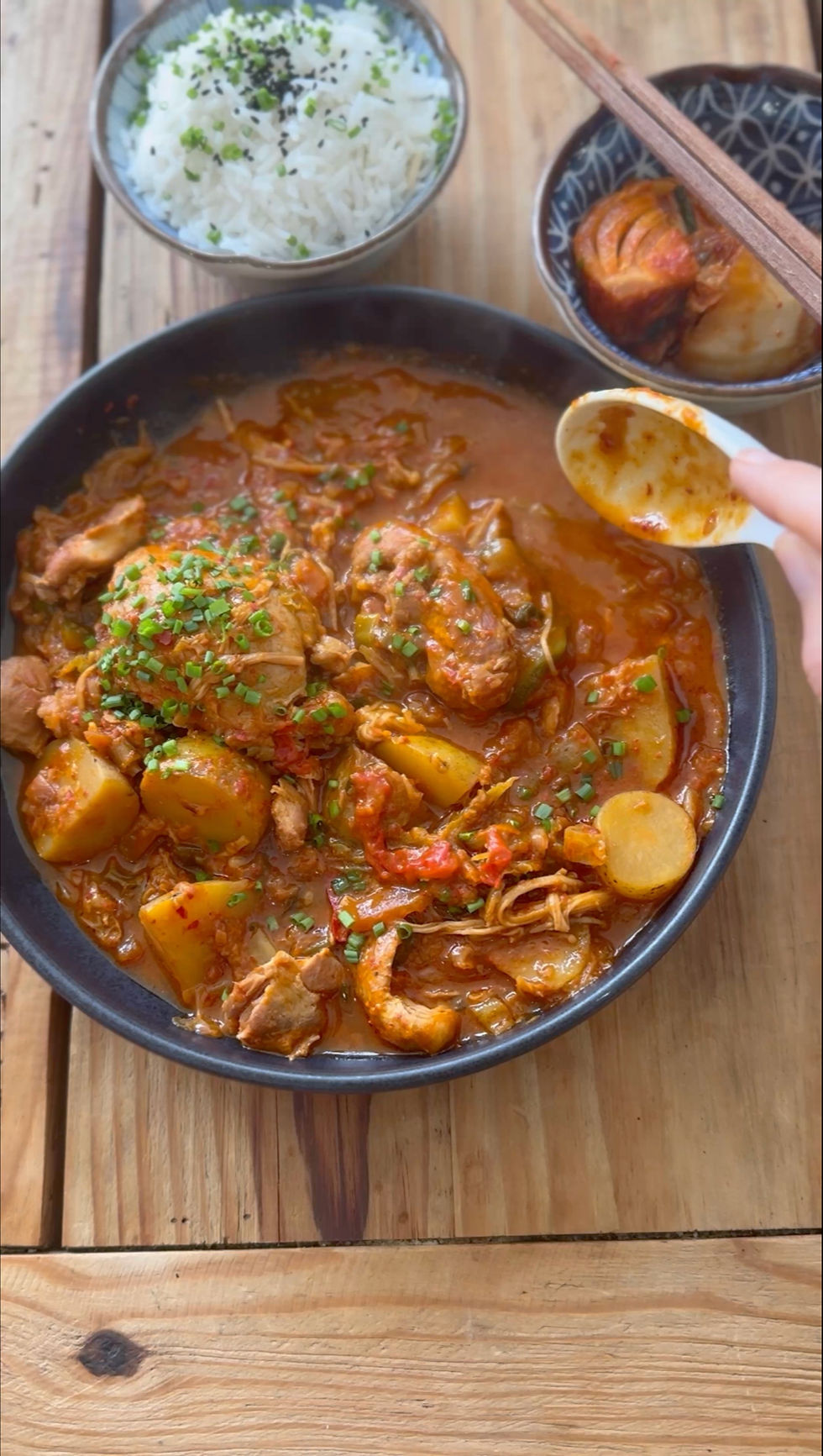 A bowl of spicy Korean braised chicken stew with a side of plain rice and kimchi.