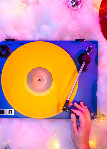 Hand on record player with yellow vinyl and festive lights