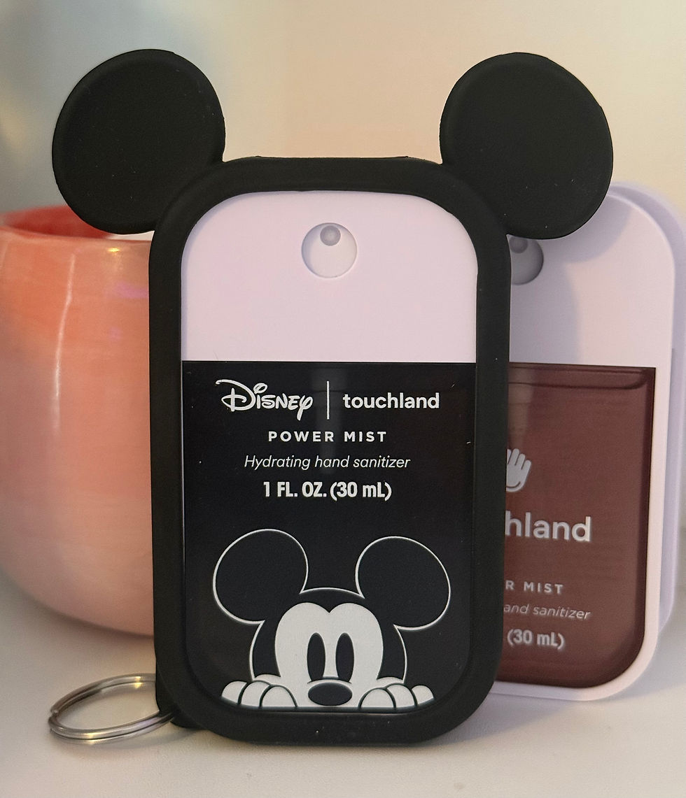 Mickey Mouse-themed hand sanitizer in a black case with ears. Text: "Disney touchland POWER MIST Hydrating hand sanitizer". Pink vase in the background.