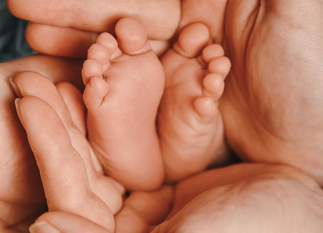 Winzige Babyfüße werden liebevoll von den Händen der Eltern gehalten, Nahaufnahme.