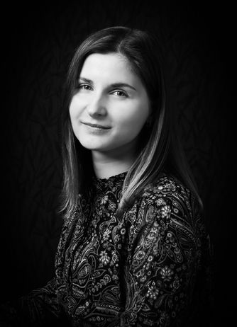 Schwarz-weiß-Porträt einer jungen Frau mit glatten, mittellangen Haaren und gemustertem Oberteil, die ruhig in die Kamera blickt und sanft lächelt.