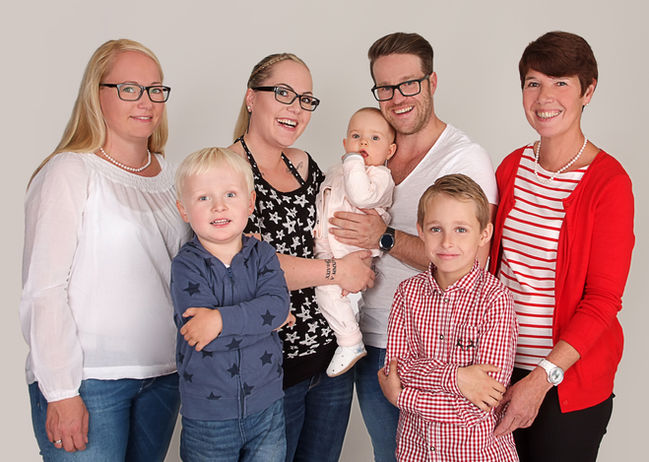  Drei Erwachsene und drei Kinder, darunter ein Baby, lachen fröhlich vor weißem Hintergrund.