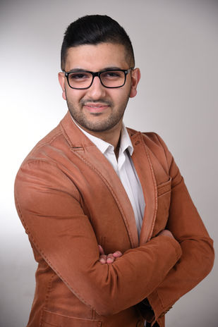 Hochwertiges Premium-Bewerbungsfoto eines Mannes mit modernem Styling und selbstbewusster Ausstrahlung. Er trägt einen stilvollen, braunen Blazer über einem weißen Hemd und eine markante Brille, die seinen professionellen Look unterstreicht. Die Pose mit verschränkten Armen vermittelt Kompetenz und Souveränität. Der dezente, helle Hintergrund sorgt für eine klare, seriöse Bildwirkung. Dieses professionelle Bewerbungsfoto aus dem Fotostudio ist ideal für Führungspositionen, Business-Profile und anspruchsvolle Bewerbungen.Bewerbungsfoto Premium in Hochformat und Farbe, stehender Mann mit Brille und verschraenkten Armen