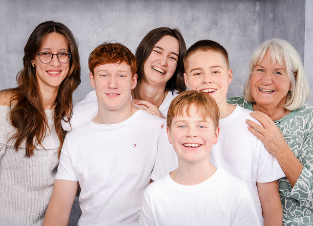 Eine Großmutter lacht gemeinsam mit fünf fröhlichen Enkeln in verschiedenen Altersstufen in die Kamera.