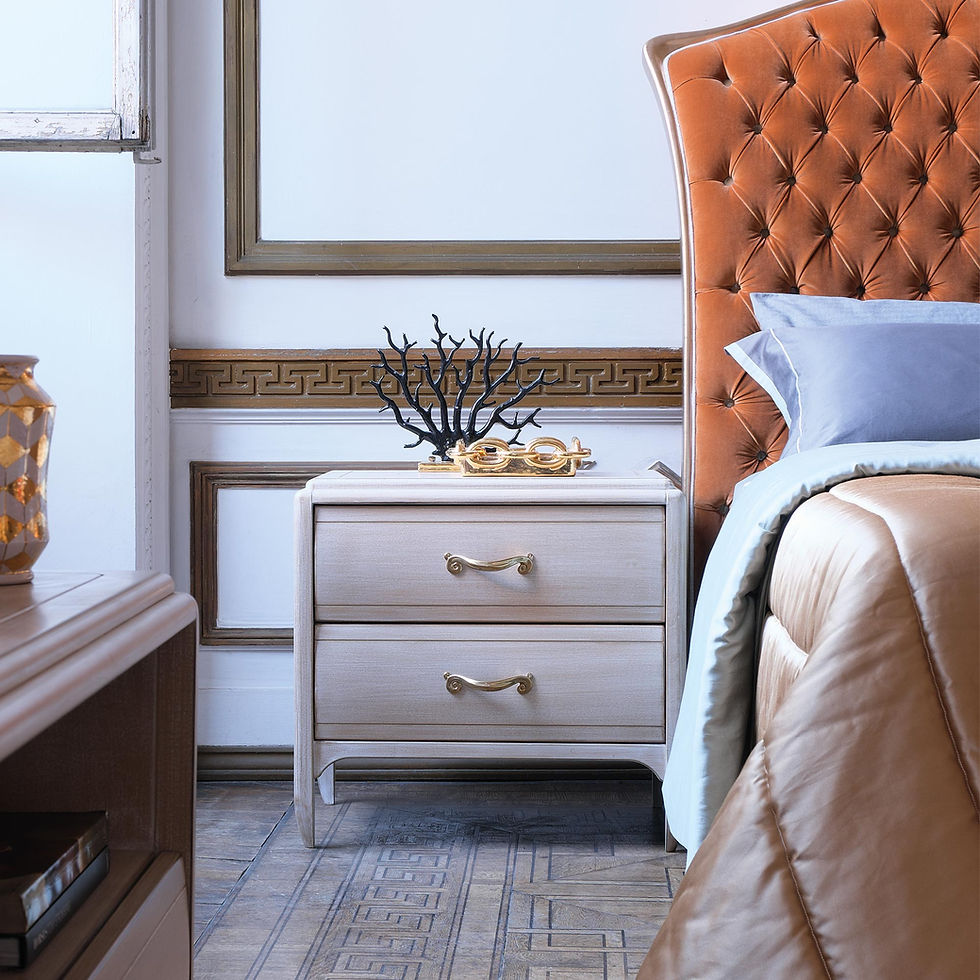 Elegant bedroom with an orange tufted headboard, beige nightstand, gold decor, and blue-grey sheets. Ornate wall trim adds classic touch. Courtesy of The Revealry, London.