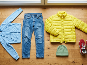 Hoodie, jeans, puffer jacket, beanie and sneakers laid flat on a wood floor