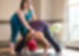 Yoga therapist and shamanic practitioner Kristi Schwickerath assists a client in a wide legged forward fold. With the lightest of touches at the lower and upper back the client is able to better percieve where their body is in a space and bring greater refinement to the experience of the shape in the physical body.