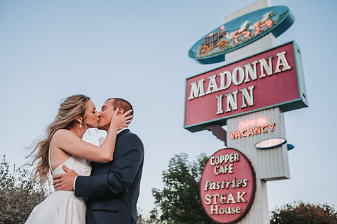 A bride and groom kiss under the Madonna Inn freeway sign