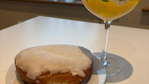 Photograph of large gin glass decorated with painted African daisy flowers containing an orange drink next to an apple danish on a plate