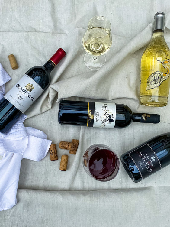 Weinflaschen, eine Stoffserviette, mehrere Korken und zwei Weingläser, eines mit Weißwein, eines mit Rotwein, auf einer Decke