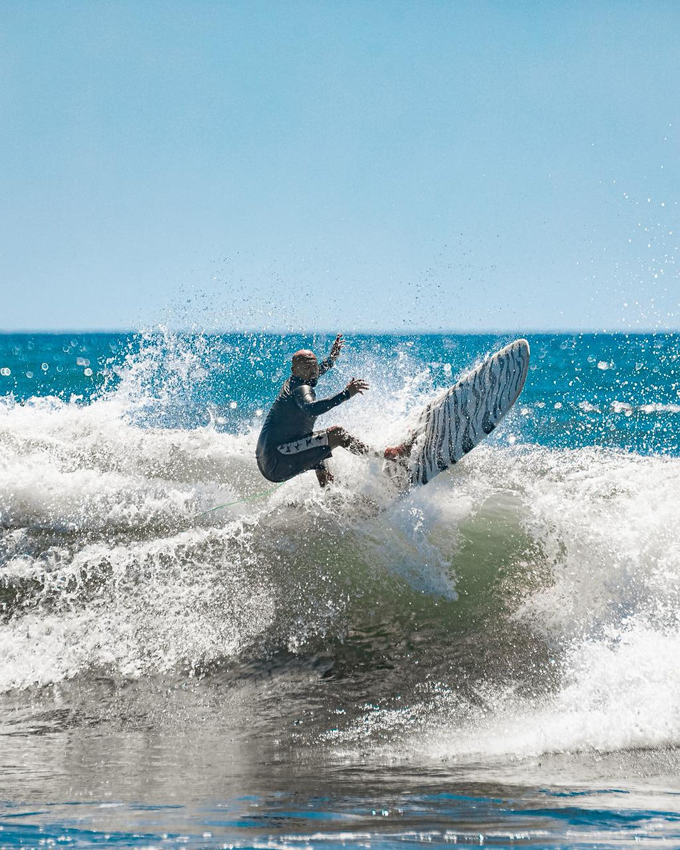 Surfer in wetsuit rides a breaking wave under a clear blue sky. Water splashes around, creating dynamic energy and excitement.