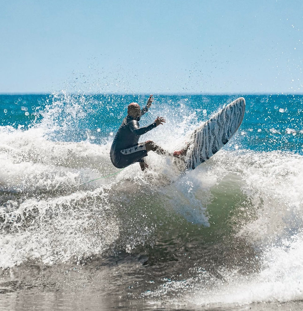 Surfer in a skillfully rides a wave, with ocean spray and a clear blue sky. The surfboard features a black-and-white pattern.