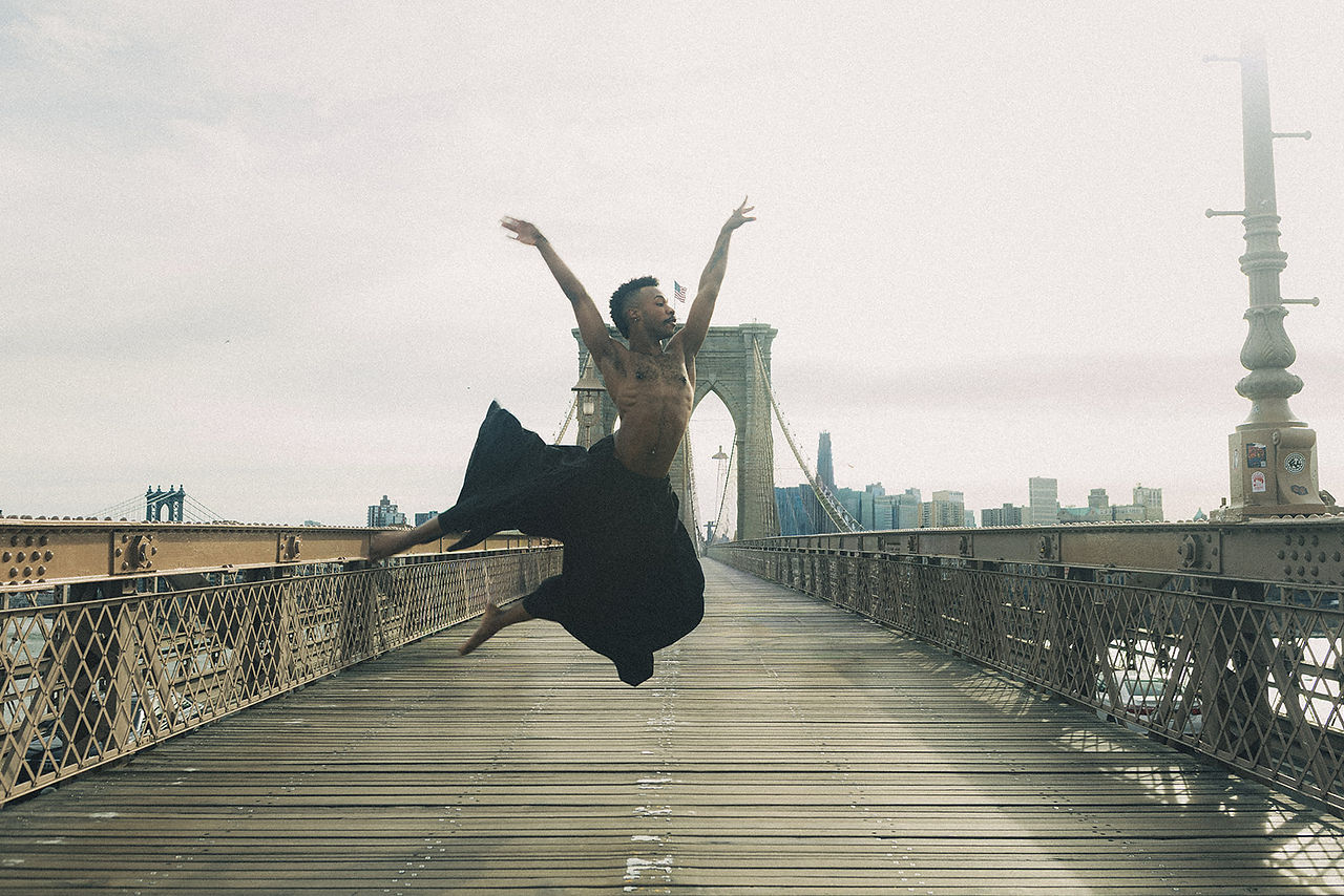 Alvin Ailey American Dance Theater inspired, contemporary dance, graceful male dancer, fluid motion, expressive storytelling, Horton Technique, dramatic stage lighting, golden hour glow, NYC rooftop, wind flowing fabric, emotional intensity, cinematic shadows, motion blur, artistic, 35mm film grain