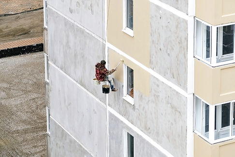 industrial-rope-access-worker-hanging-from-building-while-painting-exterior-facade-wall-in